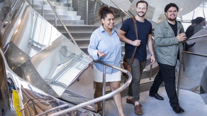 Three Indigenous students are walking on campus and engaging in casual conversation.