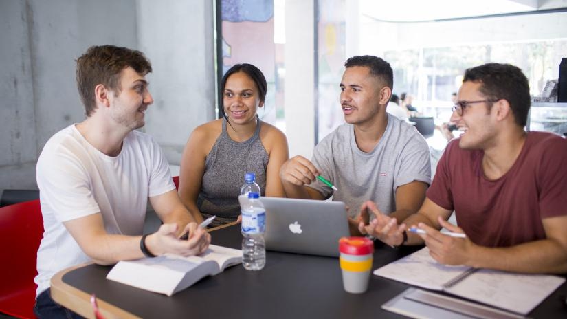 Four Indigenous students are working at a table and engaging in casual conversation.