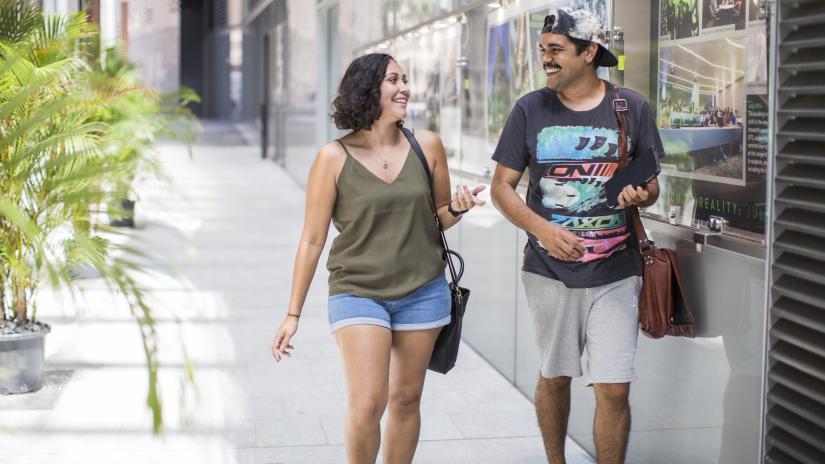 Two Indigenous students are walking outside on a footpath and engaging in casual conversation.