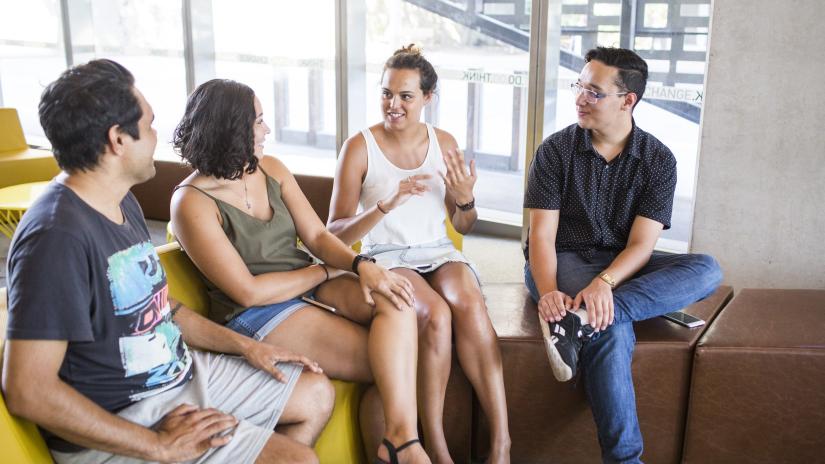 Four Indigenous students are sitting and engaging in casual conversation.