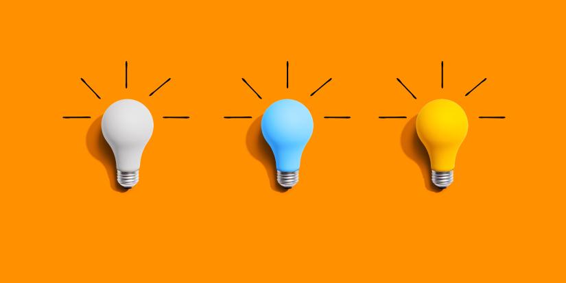 Idea and creativity concept with white, blue and yellow light bulbs laying flat on an orange background.