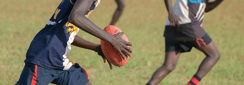 Young Indigenous men play AFL on a grassy field