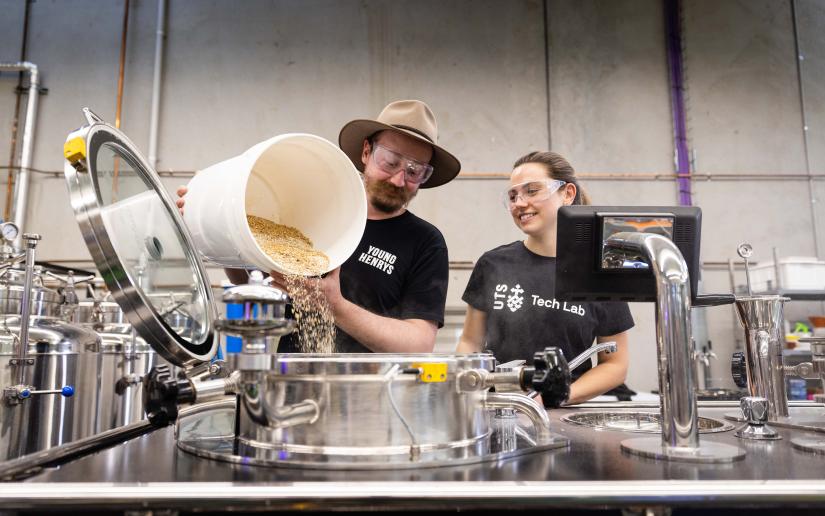 Brewing at the Centre for Advanced Manufacturing. PhD student wAn industry partner from Young Henrys is pouring ingredients into a large stainless steel with a