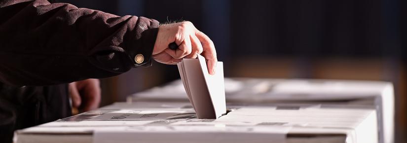 an older person places a voting paper in a polling box