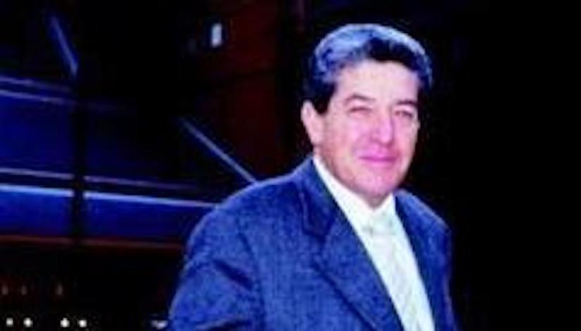 head and shoulders shot of man in suit and tie against dark background