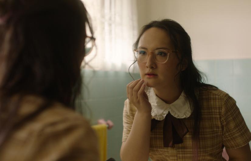A young person dressed as a school girl looks at herself in the mirror
