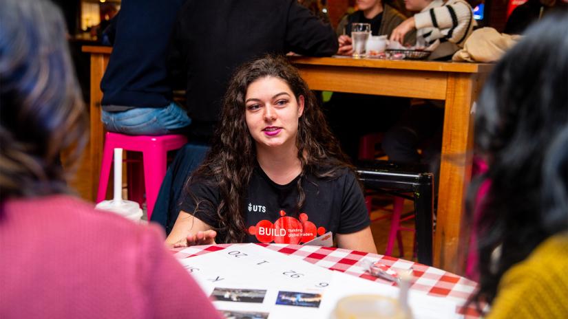 Woman in a BUILD t-shirt talking to participants at a UTS social event