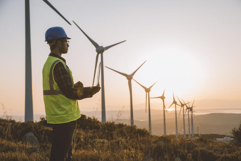 Solar engineer on laptop overlooking wind turbines