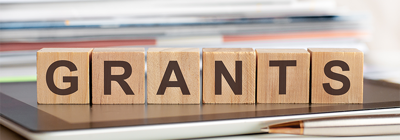 'GRANTS' spelled out on wooden blocks in capital letters. The blocks are sitting on a closed laptop computer.