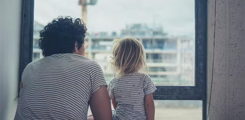 An adult and child look out of a window in an apartment