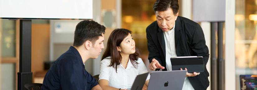 Two students looking at Apple laptops while a course instructor points to the screen.