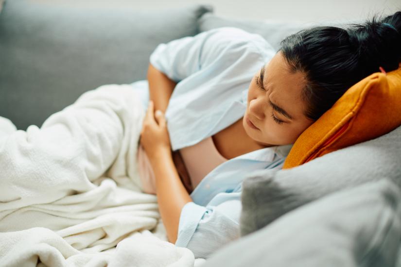 A  woman holds hands to her belly, her face expressing pain