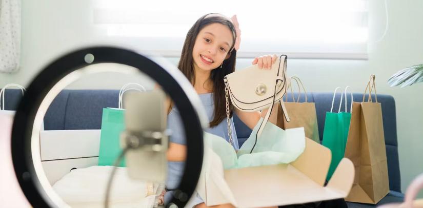 A child holds a hadbag up to a phone, smiling as if performing