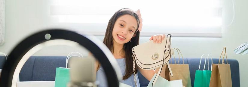 A child holds a hadbag up to a phone, smiling as if performing