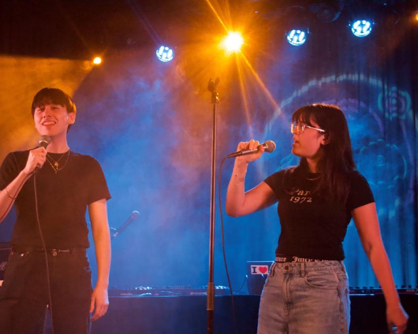 female student singing at microphone onstage with another singer