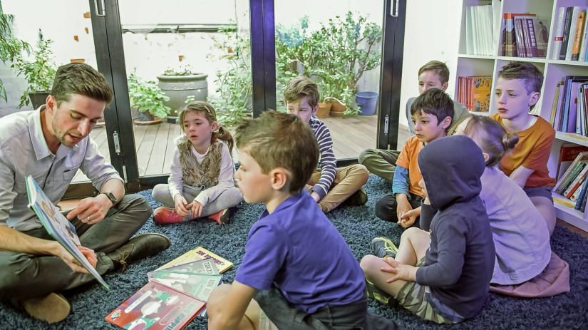 Dr Pate reads a book to a circle of primary school aged children