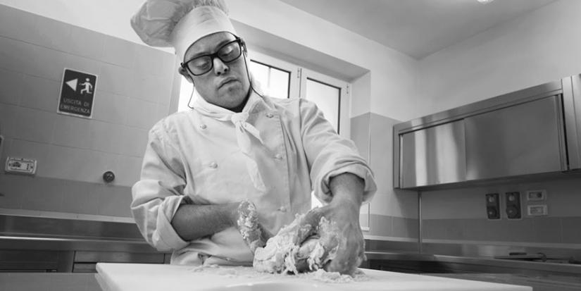 A man with down syndrome cooking in a kitchen.