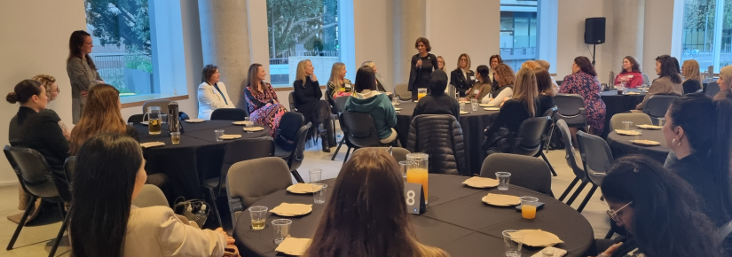 Foyer with women seated at round tables listening to a speaker