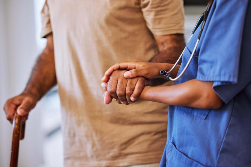 An older person walks assisted by a professional nurse or carer