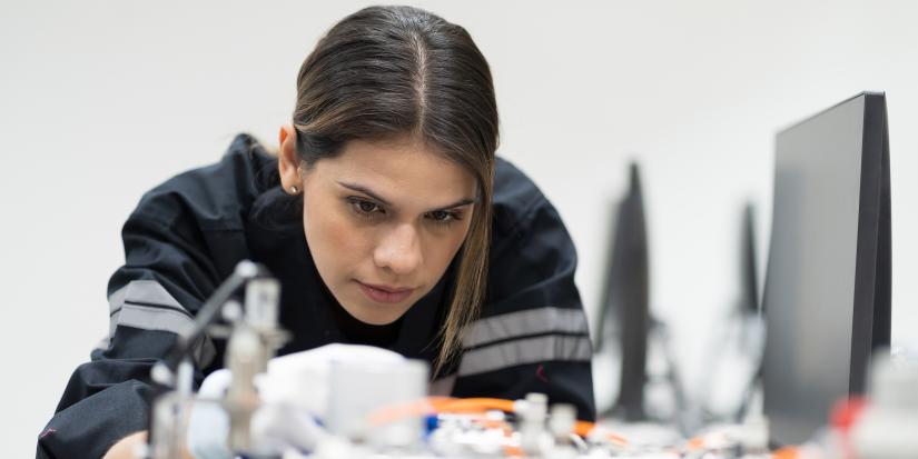 A woman working closely on electronic machinery