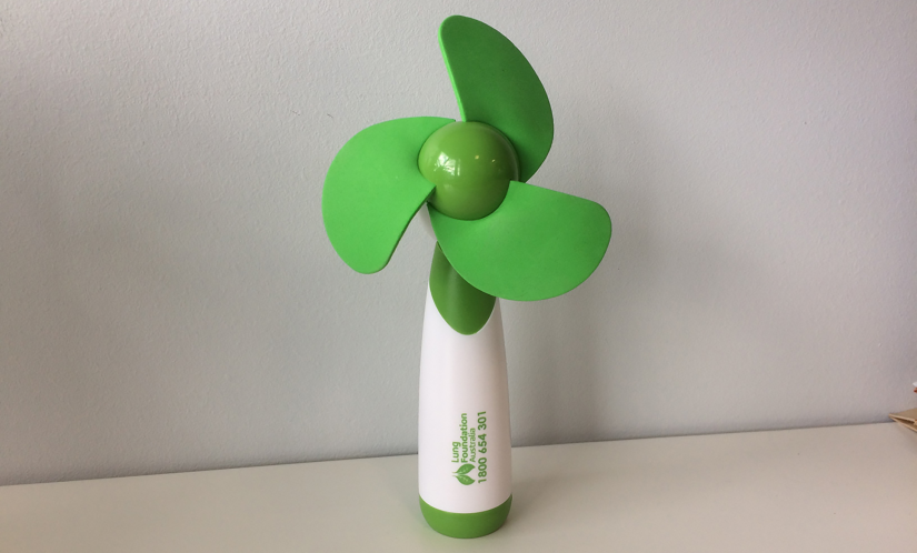 Hand-held fan with white handle and bright green blades. Text on fan reads, 'Lung Foundation Australia' next to a Lung Foundation Australia logo which is a pair of lungs in green that resemble leaves 