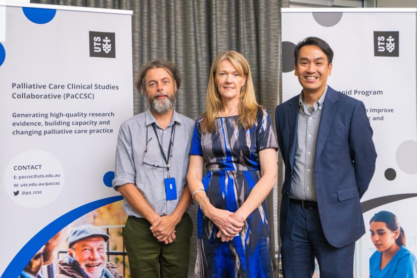 Dr Tim Luckett, Linda Brown and Professor Brian Le standing in front of the PaCCSC promotional banner. They are smiling at the camera.