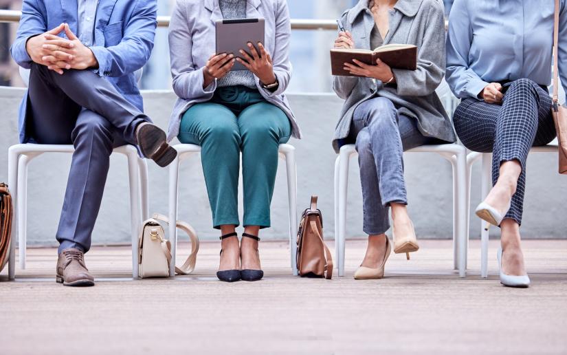 A group of unidentified workers seated in a row holding iPads, notebooks and a pen.