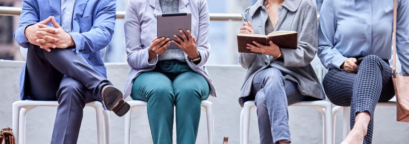 A group of unidentified workers seated in a row holding iPads, notebooks and a pen.