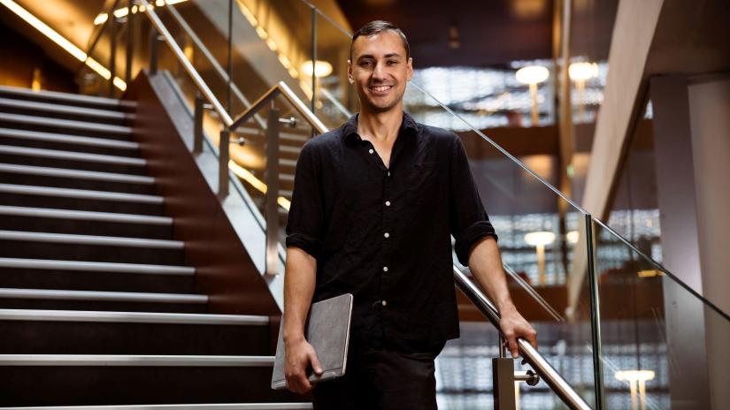 QSI SQA PhD Student Mauro Morales standing on a staircase in UTS Building 11, smiling and holding his laptop.
