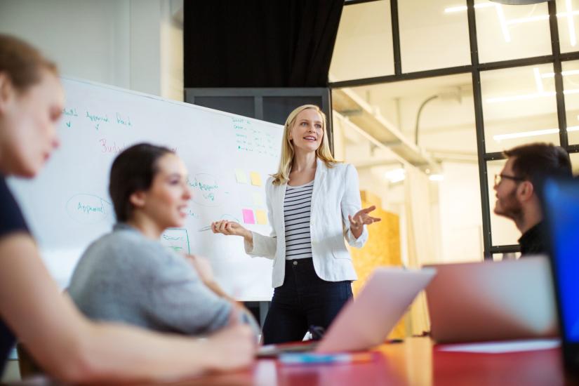 Women presenting to her work colleagues in front of a white board
