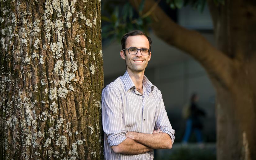 Associate Professor Harry Hobbs leans against a tree with his arms crossed.