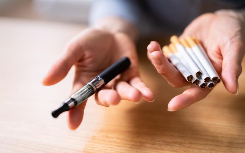 a close up of a vape in one hand and six cigarettes in the other hand