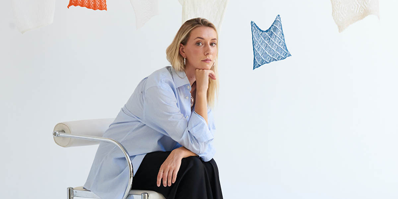 Cameron Hill sitting on a chair in front of hanging pieces of fabric