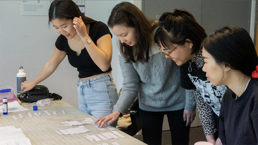 Four women collaborate around a table looking at paper cut-out tags