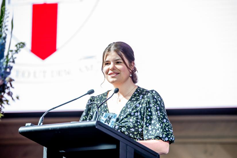 Meg stands at the lecturn and speaks to the crowd