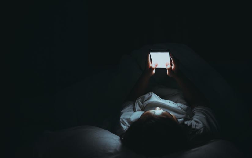 A woman looking at a mobile phone in bed. Picture: Adobe Stock