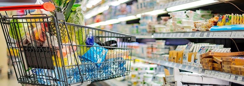 A shopping trolley filled with groceries in a supermarket aisle