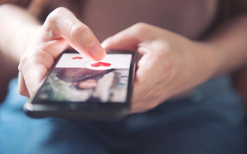 Finger of woman pushing heart icon on screen in mobile smartphone application.