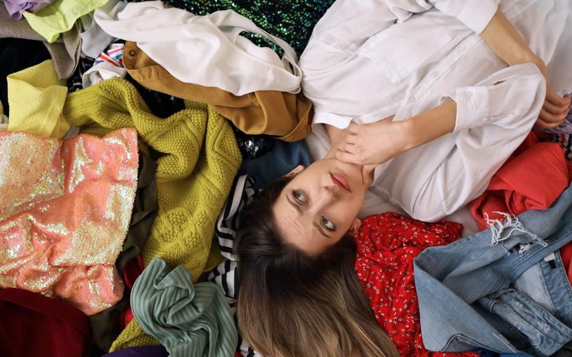 Stock picture of a young woman lying on pile of different clothes, top view. Fast fashion concept