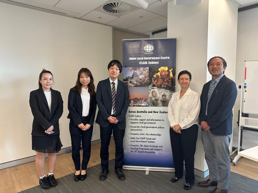 A photo of 5 people smiling and standing in front of a standin gbanner which reads "Japan Local Government Centre (CLAIR, Sydney)" 