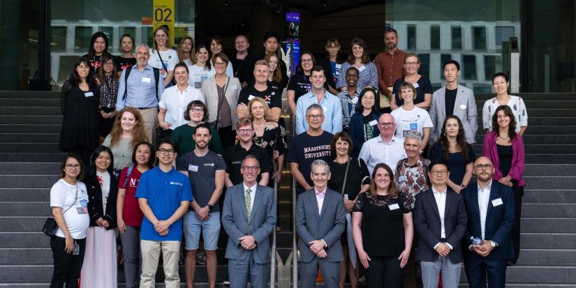 A large group of smiling people pose for a photo on the steps of UTS Building 2.