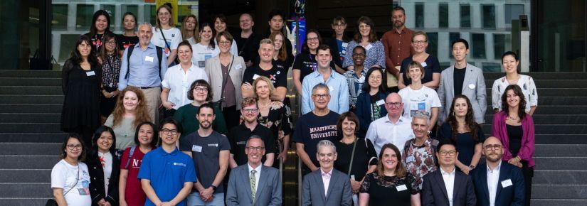 A large group of smiling people pose for a photo on the steps of UTS Building 2.