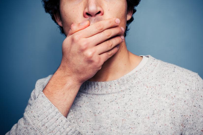 Shocked young man with his hand on his mouth.