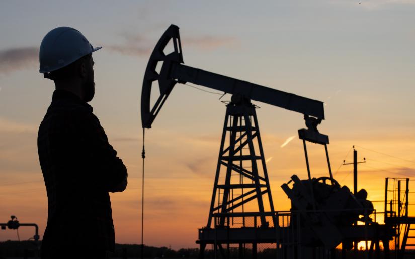 Stock picture of the silhouette of a young man in a construction helmet against the background of a working oil pump