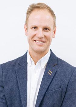 Jeremy Basset smiling and looking at the camera in a blue coloured tailored jacket with a white business shirt