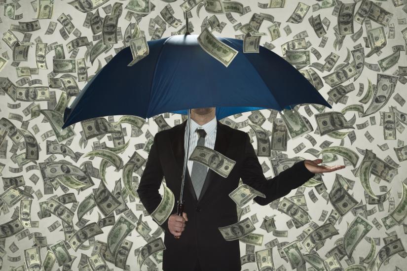 A suited person stands holding an umbrella, cash raining down around them