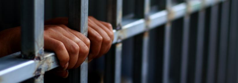 hands on bars in a jail. Adobe Stock