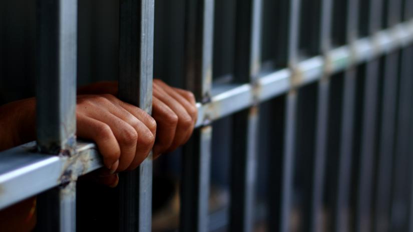 hands on bars in a jail. Adobe Stock