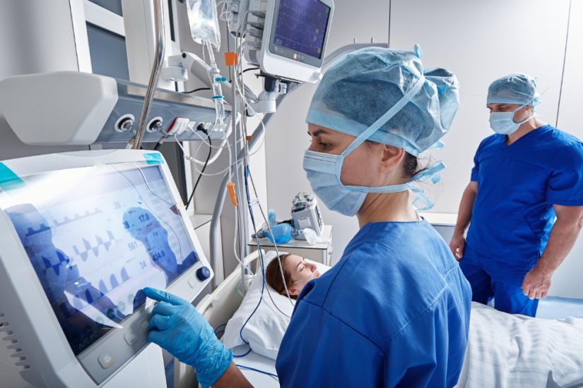 Hospital nurses checking on woman patient at intensive care unit and monitoring her health with medical equipment and sensors.