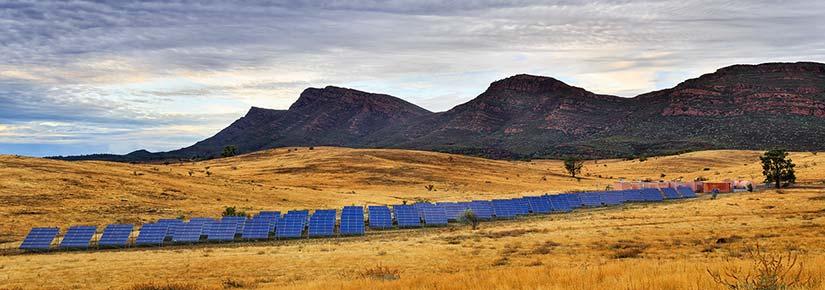 solar panels in a grassy landscape, hills and clouds in background